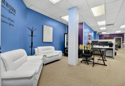 Lounge area with modern white seating, blue walls, and a view into the open-plan office space.