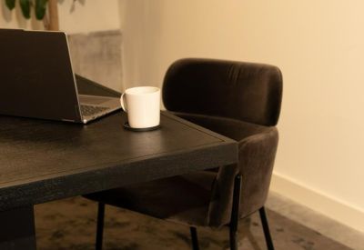Close-up of a dark wood desk with a laptop and coffee mug in a cozy workspace.