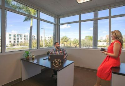 Private corner office featuring large windows with palm tree views and two people collaborating.