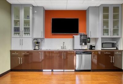 Modern breakroom with wood-style flooring, brown cabinetry, and an orange feature wall.