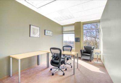 Bright corner office with large windows, light wood desks, and ergonomic chairs.