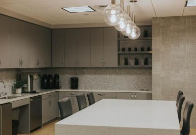 Modern breakroom kitchen with grey cabinetry and globe pendant lighting.