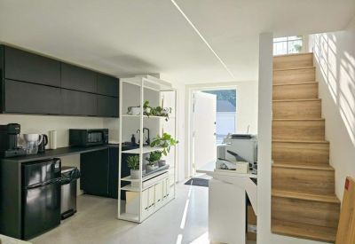 Kitchenette area with black cabinetry, a white shelving unit, and wooden stairs.