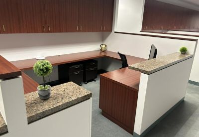 Reception desk area with warm wood finishes, granite countertops, and decorative greenery.