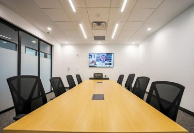 Professional boardroom with a long wooden table, ergonomic chairs, and video conferencing screen.