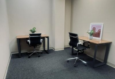 Windowless two-person office suite with wooden desks and black chairs.
