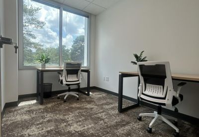 Bright private office featuring two desks and a large window with natural light.