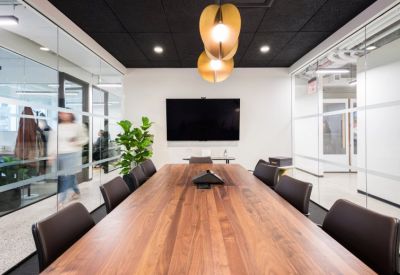 Professional boardroom with a long wood-grain table, dark leather chairs, and glass walls.