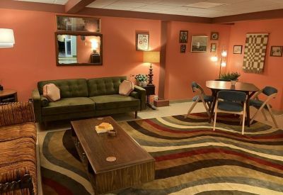 Retro lounge with warm orange walls, a green velvet sofa, and a wavy patterned rug.