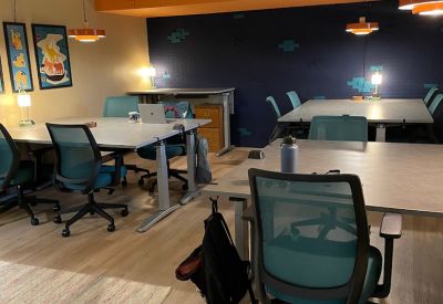 Modern coworking space with teal ergonomic chairs and height-adjustable desks.