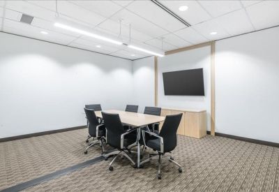 Modern conference room with a large screen, light wood table, and six black chairs.