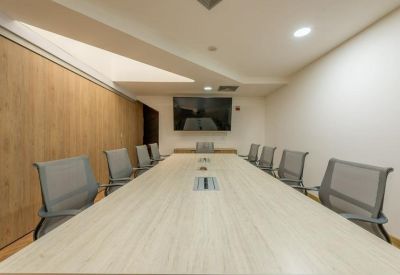 Sleek, minimalist boardroom with a long light-wood table and grey mesh chairs.