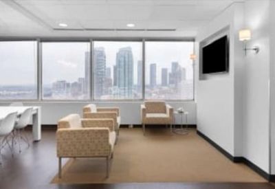 Modern lounge area with comfortable tan armchairs and city skyline views.