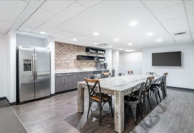 Modern communal kitchen and breakout area with a large wooden table and stainless steel fridge.