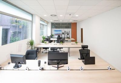 Bright, open-plan coworking space with large windows and multiple computer workstations.