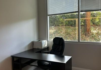 L-shaped black desk in a private workspace with light wood-style flooring.