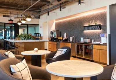 Communal kitchen area with a beverage station, marble-topped tables, and grey armchairs.