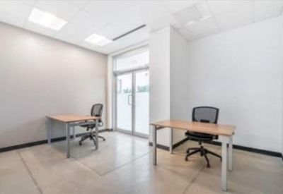 Bright private office featuring two minimalist wooden desks and ergonomic mesh chairs.