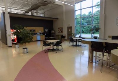Bright communal break area with café seating, large windows, and a vending machine.