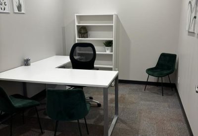Private L-shaped desk setup with green velvet chairs and a white bookshelf.