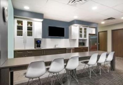 Bright office kitchen and breakroom with a long breakfast bar and white modern seating.