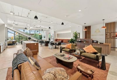 Spacious communal lounge and reception area with warm lighting, leather sofas, and a branded Industrious front desk.