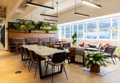 Spacious coworking lounge with a long stone table, leather banquette seating, and vibrant plant wall.