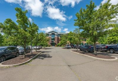 Wide view of the office parking lot surrounded by mature green trees under a blue sky.
