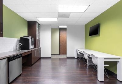 Modern breakroom with a lime green wall, white dining tables, and coffee station.