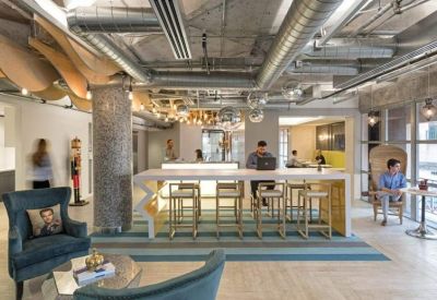 Vibrant communal lounge with exposed ductwork, a long high-top table, and plush armchairs.