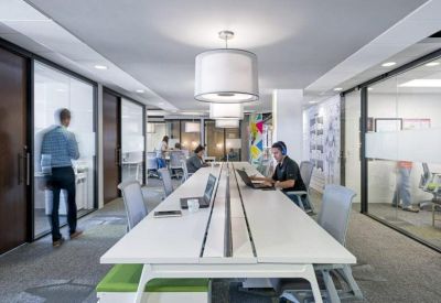 Bright open-plan office featuring long white workstations and large drum pendant lighting.