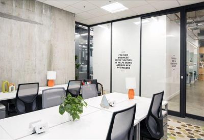 Modern shared workspace with large white tables and black mesh chairs.