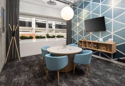 Small meeting room with a round wooden table, blue chairs, and geometric wall pattern.