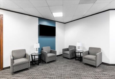 Reception lounge with grey armchairs, side tables, and a wall-mounted television.