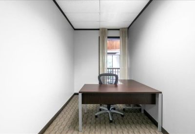 Private windowed office with a dark wood L-shaped desk and ergonomic chair.