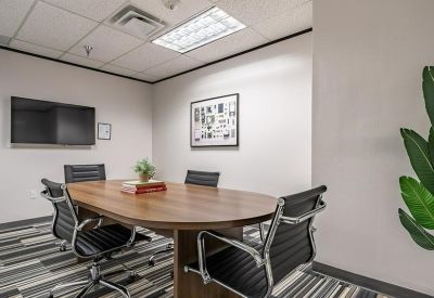 Small meeting room with an oval wood table, black leather chairs, and wall-mounted television.