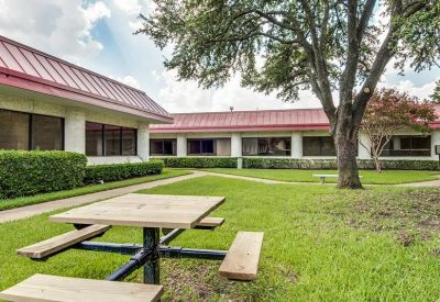 Outdoor picnic table on a green lawn surrounded by mature trees and office buildings.