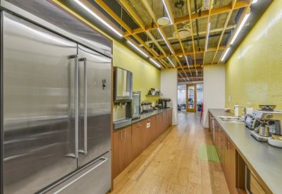Bright office kitchen featuring yellow tile walls and stainless steel appliances.