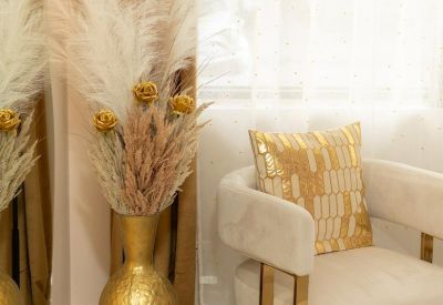Elegant seating area with a white velvet chair, gold accents, and a large pampas grass arrangement.
