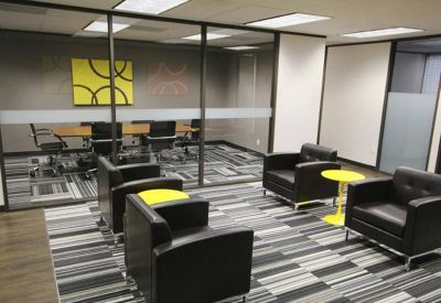 Modern lounge area with black leather armchairs and bright yellow side tables on a striped carpet.