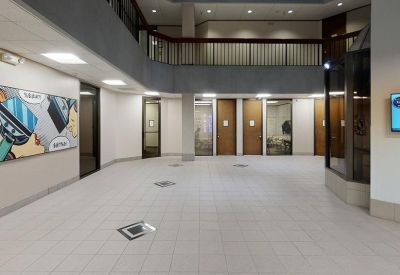 Spacious building lobby with white tiled floors, wood-trimmed doorways, and a second-floor balcony.