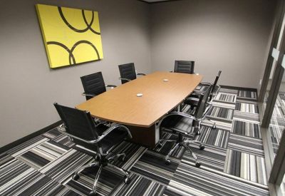 Professional conference room with a large wooden table, black chairs, and yellow wall art.