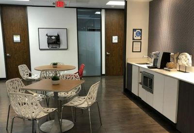 Breakout area featuring patterned white chairs around wooden tables next to a kitchenette.