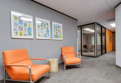 Bright waiting area featuring two orange armchairs and colorful framed wall art.