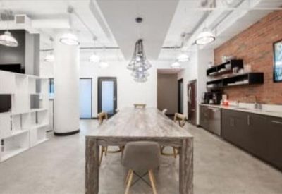 Modern communal kitchen and dining area featuring a brick wall and long wooden table.