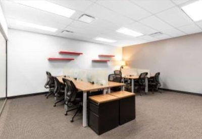 Open coworking area with several desks, black chairs, and red wall shelves.