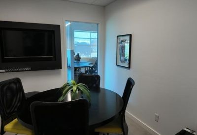 Small private meeting room with a round black table, wall-mounted screen, and yellow accents.