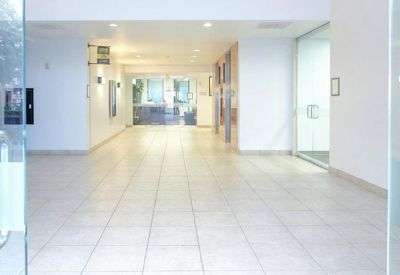Bright, spacious building lobby with white walls and polished tile flooring leading to glass doors.