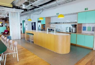Modern office pantry with a long wooden breakfast bar and mint green storage cabinets.