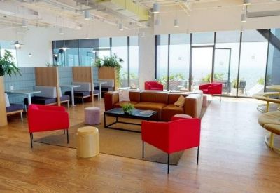 Sun-drenched lounge with red velvet chairs, a leather sofa, and floor-to-ceiling city views.